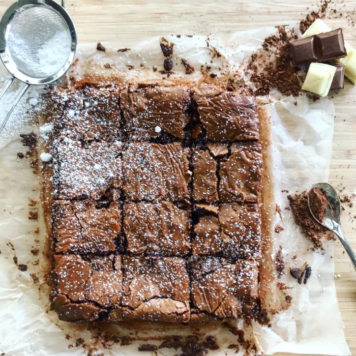 Chocolate brownies, sieve and chocolate on chopping board