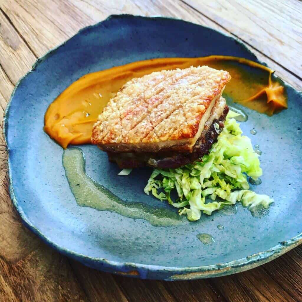 Crispy pork, sweet potatoes & cider Crispy pork belly, sweet potato puree, cabbage & cider sauce on a plate