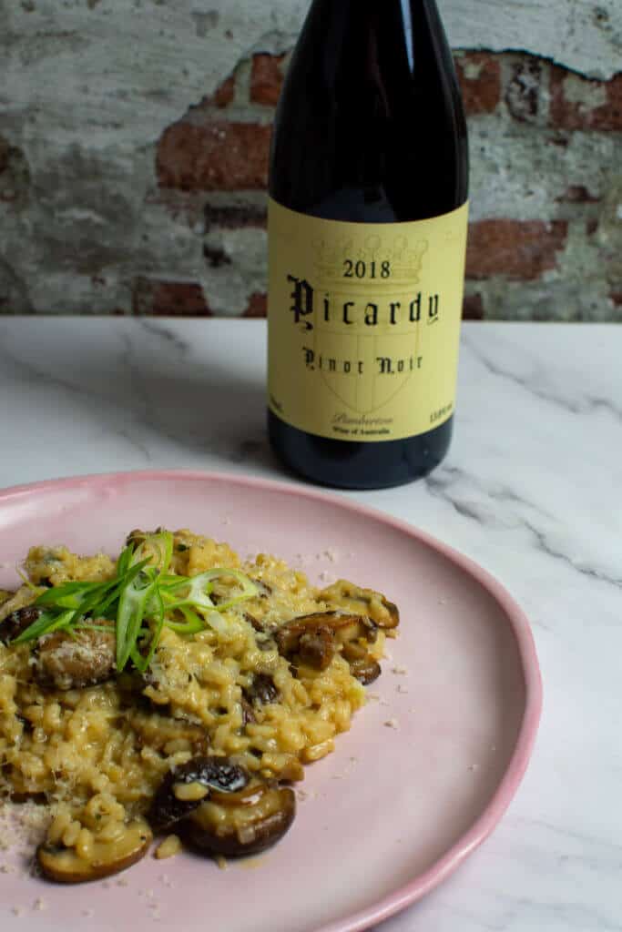 wild mushroom risotto on pink plate with a btl of picardy pinot noir