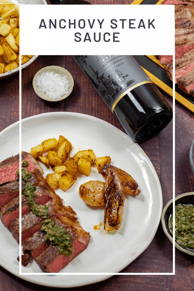 Cooked steak topped with anchovy steak sauce & potatoes on a plate. Barossa shiraz beside it