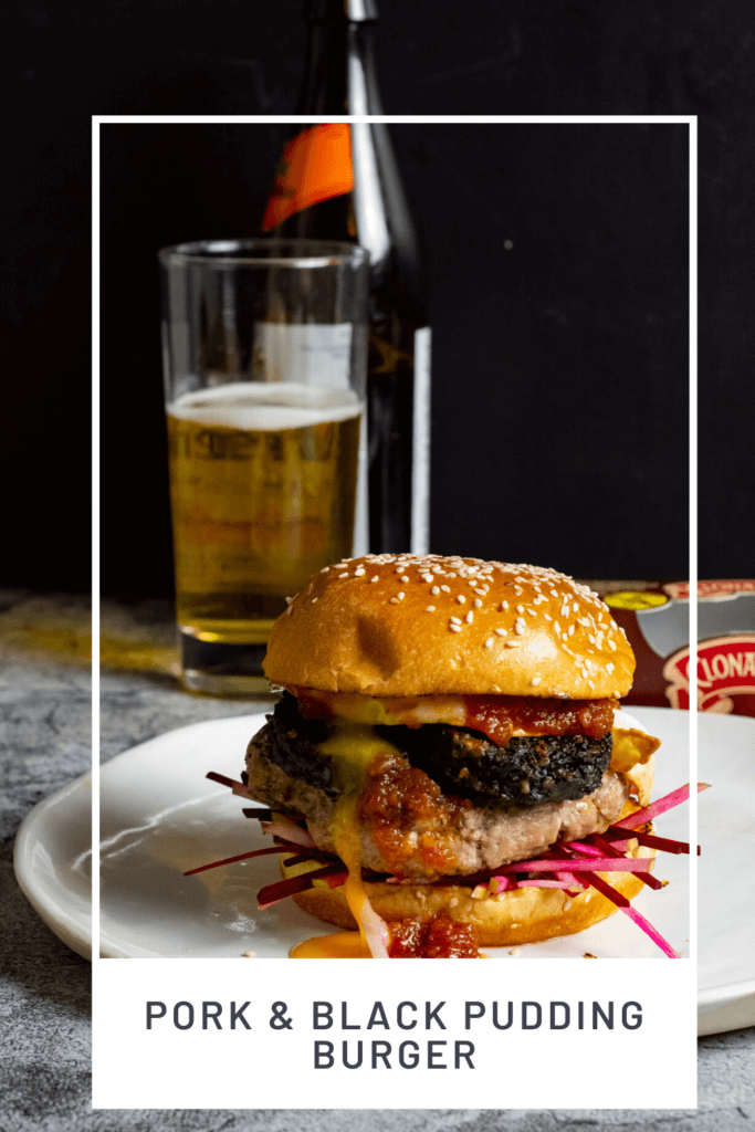 Pork & black pudding burger on a white plate with a beer in background