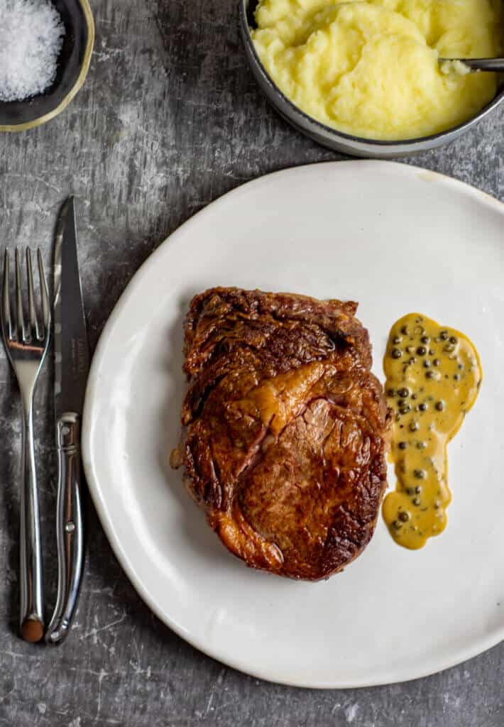 Rib fillet, pepper sauce, mashed potatoes and cutlery on a table