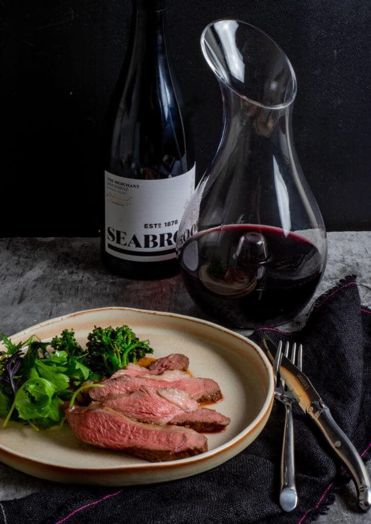 Seabrook wine shiraz, wine decanter, BBQ lamb, romesco sauce & charred broccolini on a table