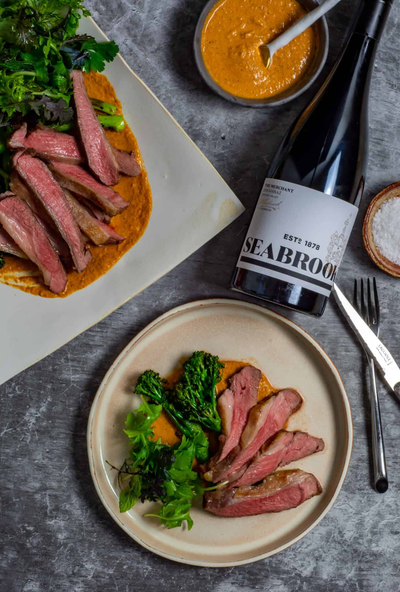 Seabrook wine shiraz, BBQ lamb, romesco sauce & charred broccolini on a table
