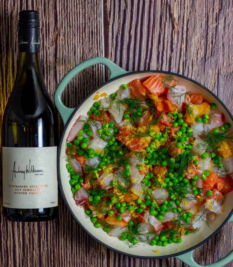 Raw fish, peas & dill in a pan for fish pie and a bottle of wine