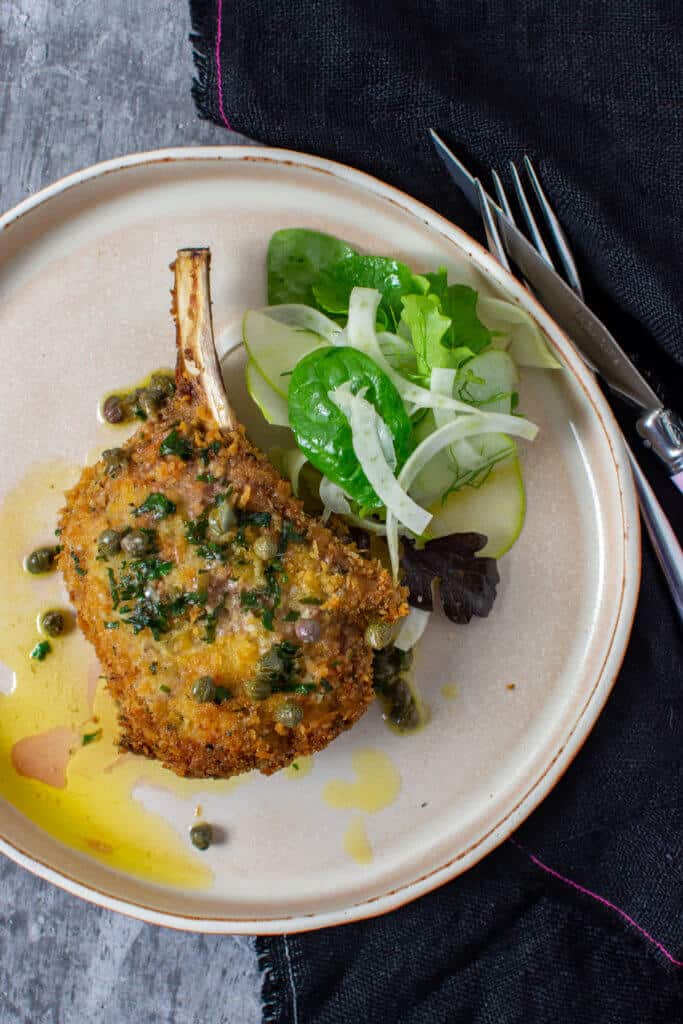 crumbed veal cutlet, lemon caper sauce, salad on a plate with cutlery beside it