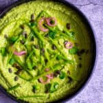 black bowl with avocado & pea hummus topped with pickled onions, pepitas, herbs & snowpeas