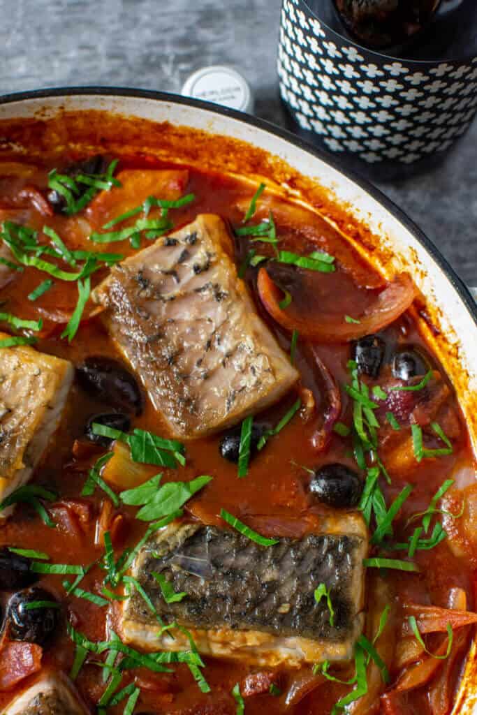 spanish fish stew in a white casserole dish and a bottle of heirloom wine