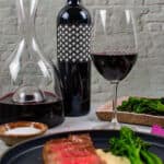 steak & onion soubise on a plate, decanter, glass of wine and bottle heirloom shiraz