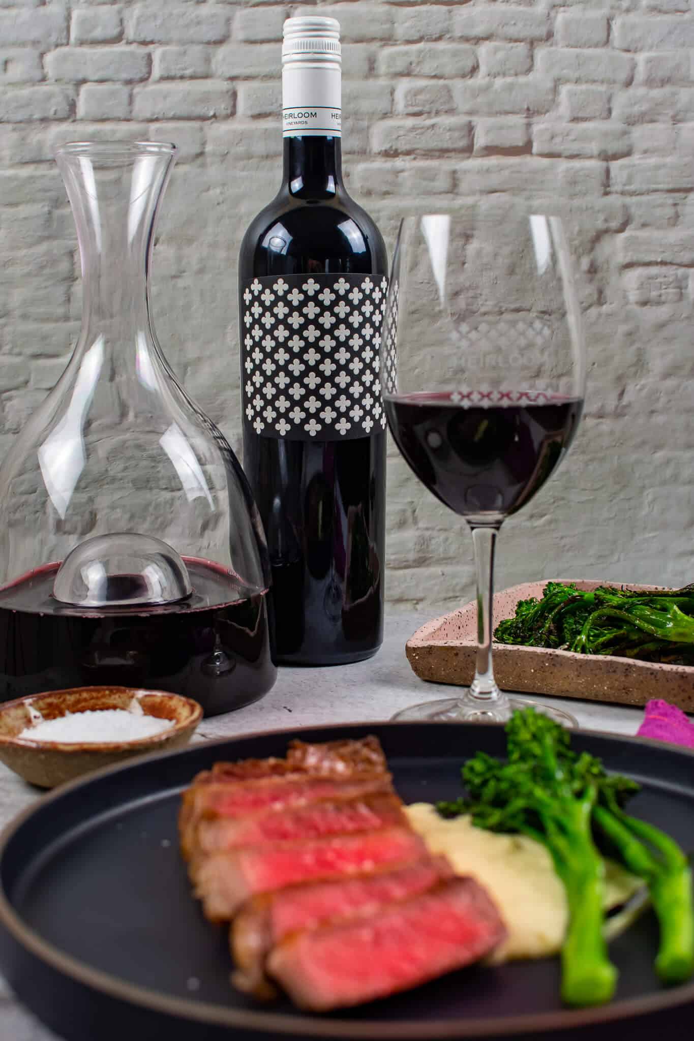 steak & onion soubise on a plate, decanter, glass of wine and bottle heirloom shiraz