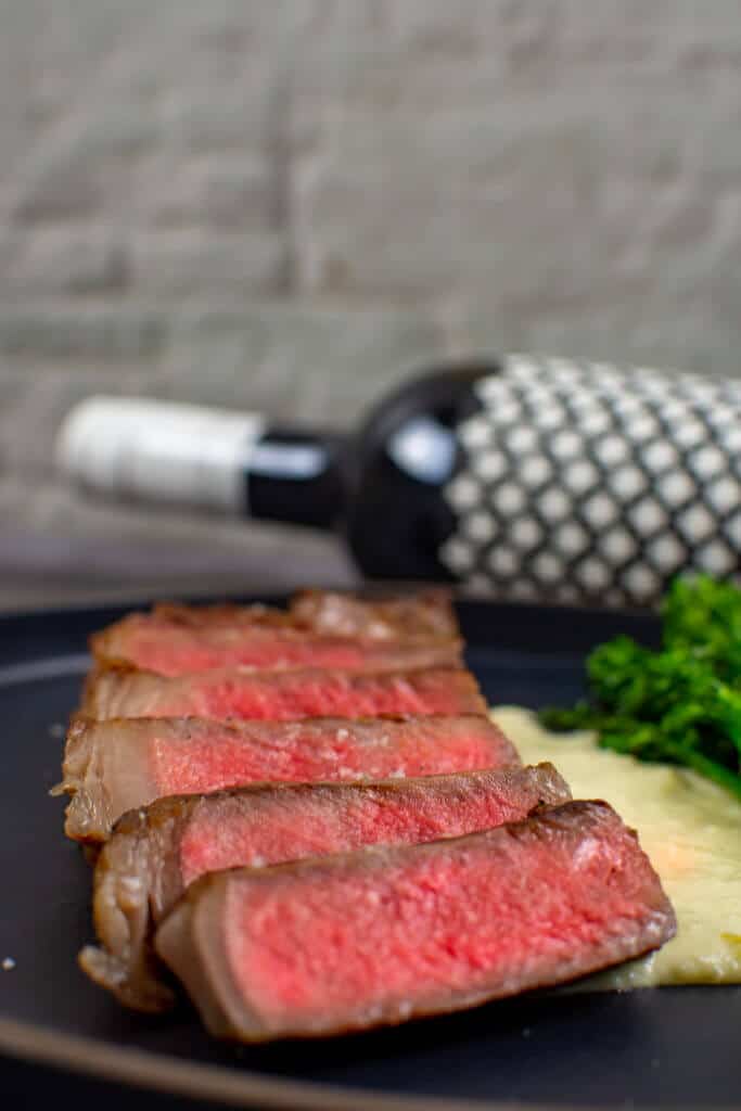 medium rare striploin on a plate. Bottle of heirloom shiraz in background