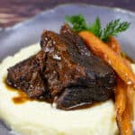 mushroom braised short ribs, cauliflower puree & carrots in a bowl on wooden table