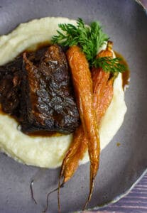 mushroom braised short ribs, cauliflower puree & carrots in a bowl on wooden table