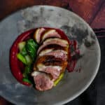 Duck breast, rhubarb ketchup & asian greens in a made of australia bowl on a table
