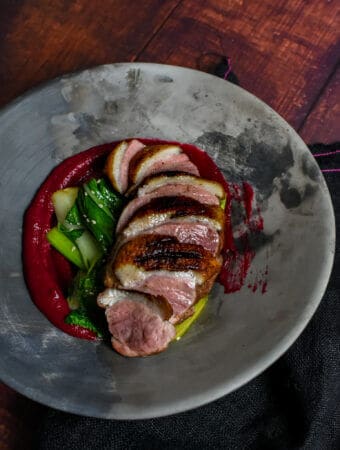 Duck breast, rhubarb ketchup & asian greens in a made of australia bowl on a table
