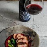 Duck breast, rhubarb ketchup & asian greens in a made of australia bowl on a table with heirloom pinot noir