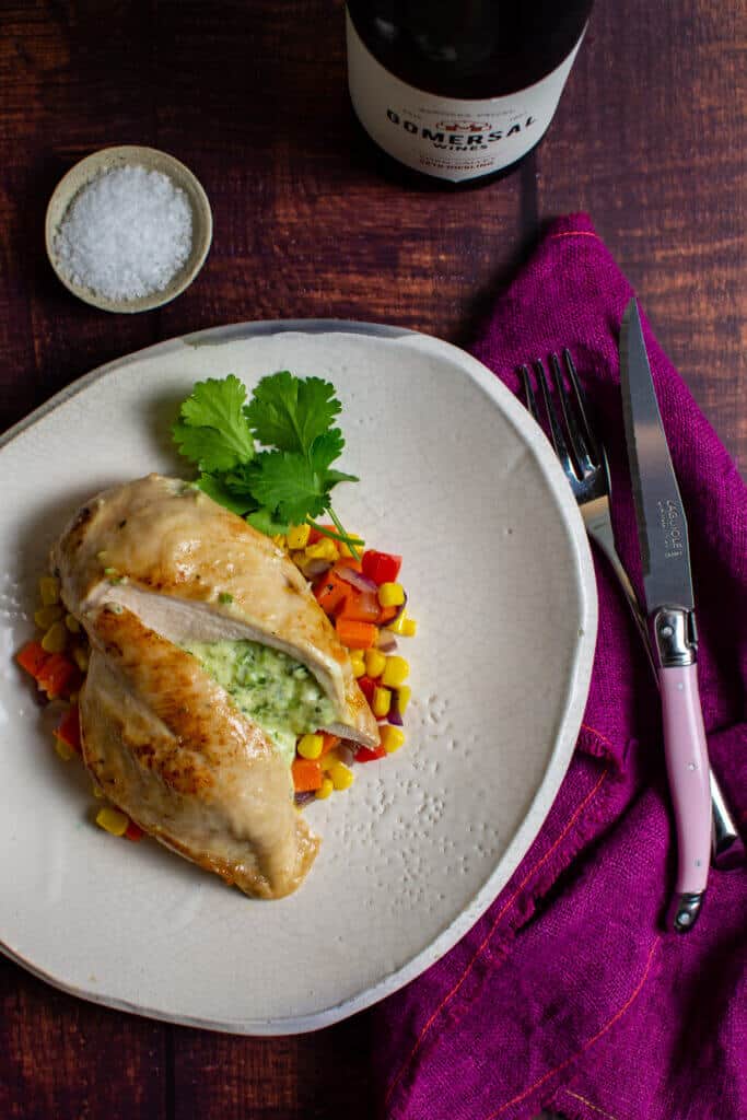 jalapeno popper stuffed chicken & corn hash on a plate, pink napkin, laguiole steak knife and bottle of gomersal wine