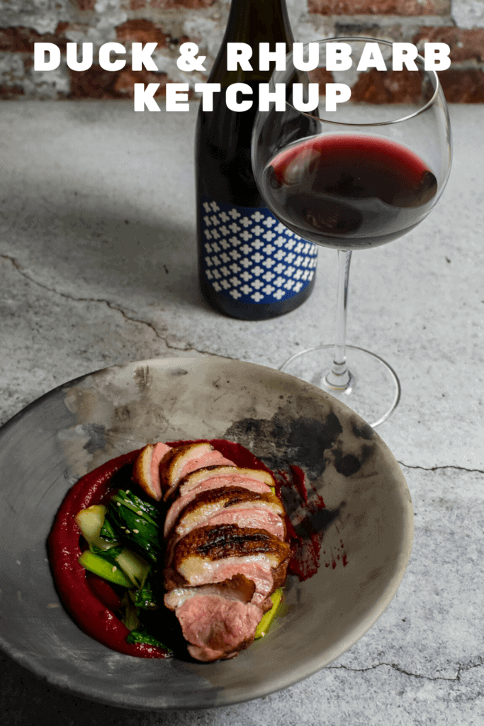 Duck breast, rhubarb ketchup & asian greens in a made of australia bowl on a table with heirloom pinot noir