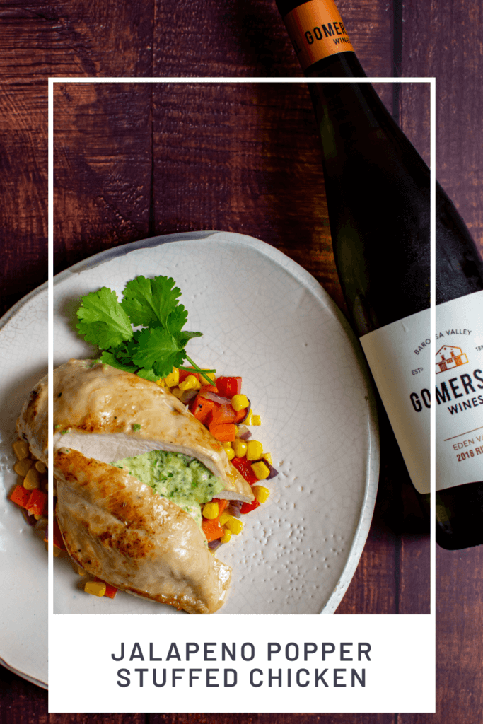 jalapeno popper stuffed chicken on white plate with corn hash and a bottle of gomersal wine