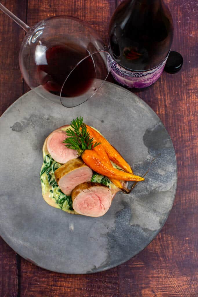pork tenderloin, creamed spianch & carrots on a made of australia plate with a btl of mazzini pinot noir
