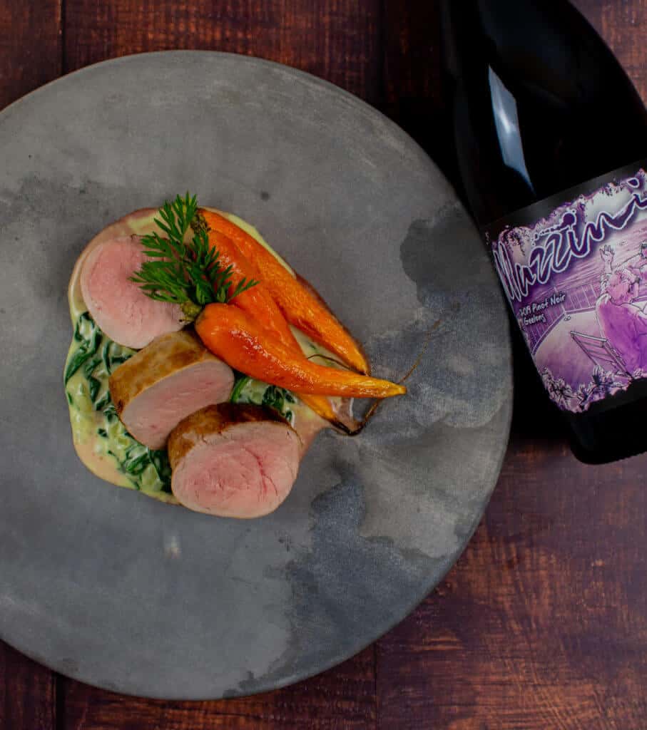 pork tenderloin, creamed spianch & carrots on a made of australia plate with a btl of mazzini pinot noir