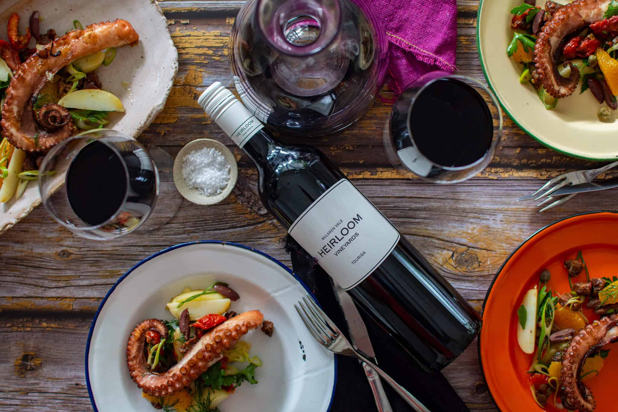 birds eye view of grilled octopus salad, wine glasses, cutlery and bottle of heirloom wine