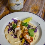 grilled fish taco on a plate with a bottle of marri wood park pet nat behind it