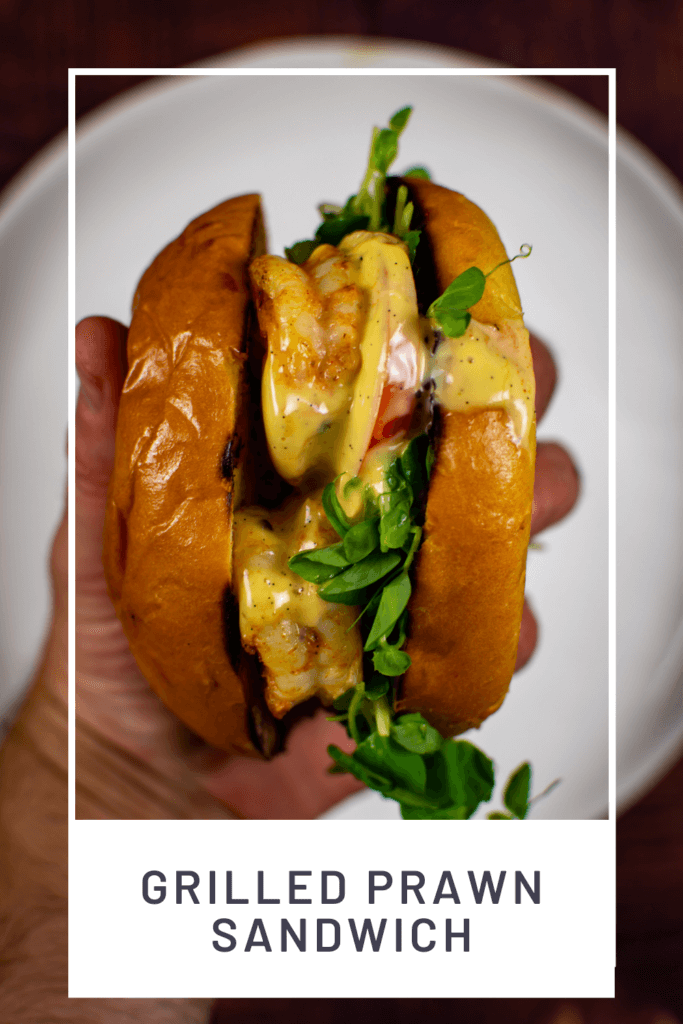 someone holding a griled prawn sandwich above a white plate