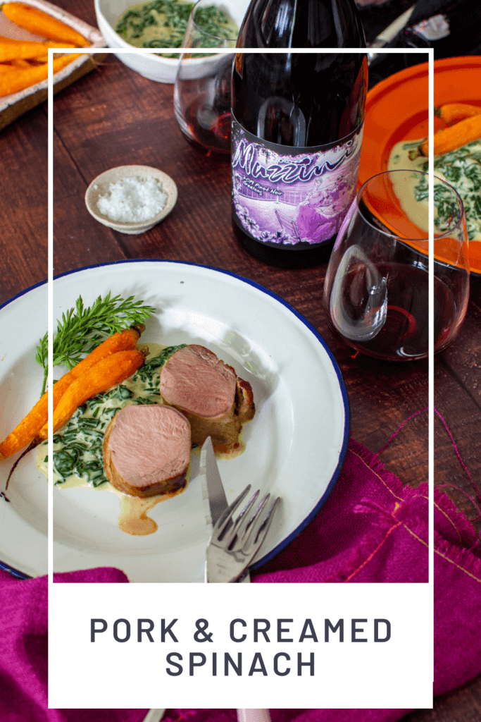 2 plates of pork tenderloin, creamed spinach & carrots, mazzini pinot noir and cutlery on a table