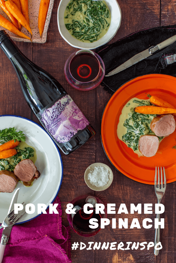 2 plates of pork tenderloin, creamed spinach & carrots, mazzini pinot noir and cutlery on a table