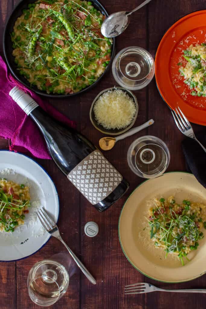 plates of pea & pacon risotto, heirloom chardonnay & wine glasses on a table