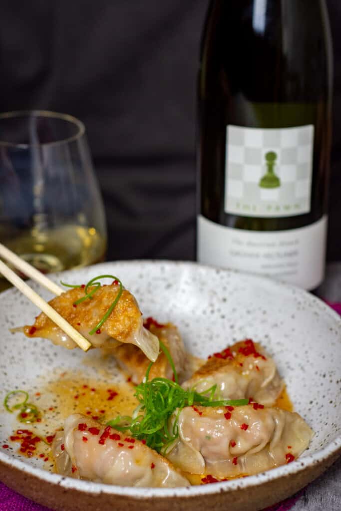 someone eating pork & prawm dumplings with chopsticks and a bottle of The Pawn Wine Co gruner veltliner in background
