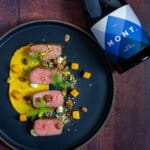 lamb, smoked squash puree, & pistachio dukkah on a black plate with mont wines syrah next to it