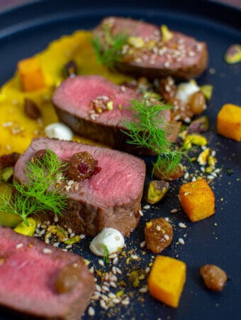 lamb, smoked squash puree, & pistachio dukkah on a black plate