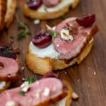 duck crostinis with cherries & goat cheese on wooden chopping board