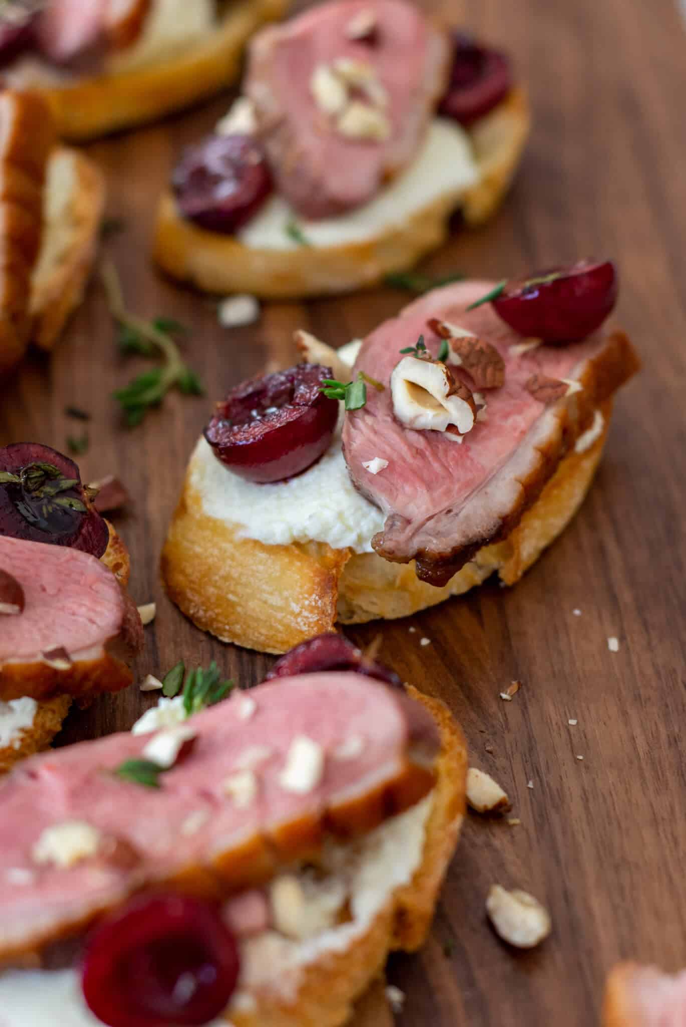 duck crostinis with cherries & goat cheese on wooden chopping board