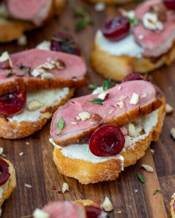 duck crostinis with cherries & goat cheese on wooden chopping board