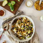 charred brussel sprouts & pangrattato in a bowl with a chopping board, brussel sprouts in the background