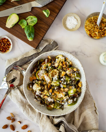 charred brussel sprouts & pangrattato in a bowl with a chopping board, brussel sprouts in the background
