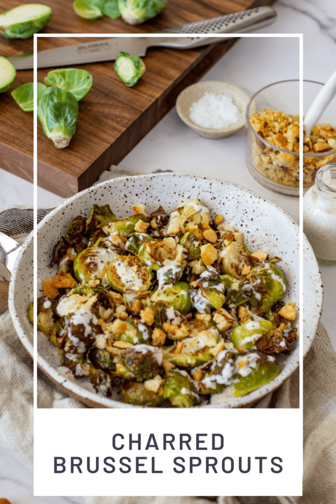 charred brussel sprouts & pangrattato in a bowl with a chopping board, brussel sprouts in the background