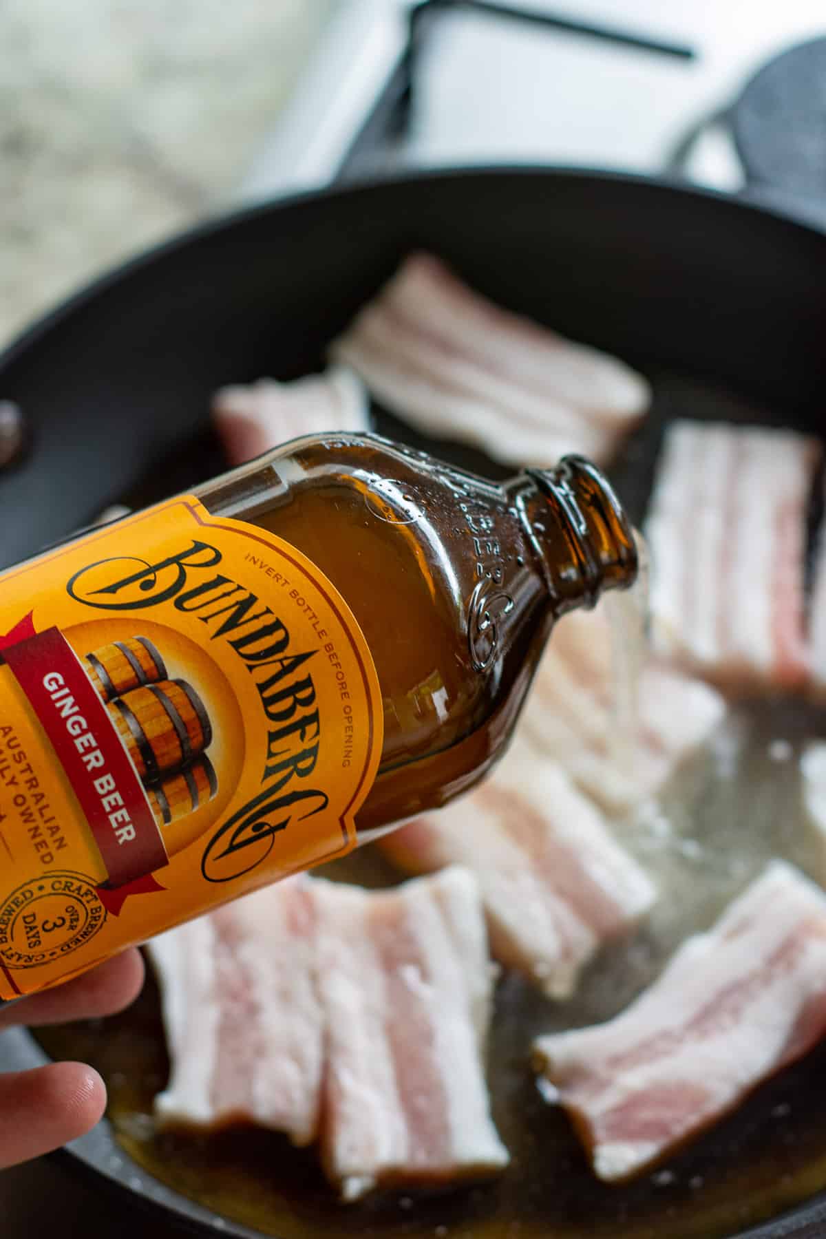 ginger beer being poured into a frying pan with pork belly