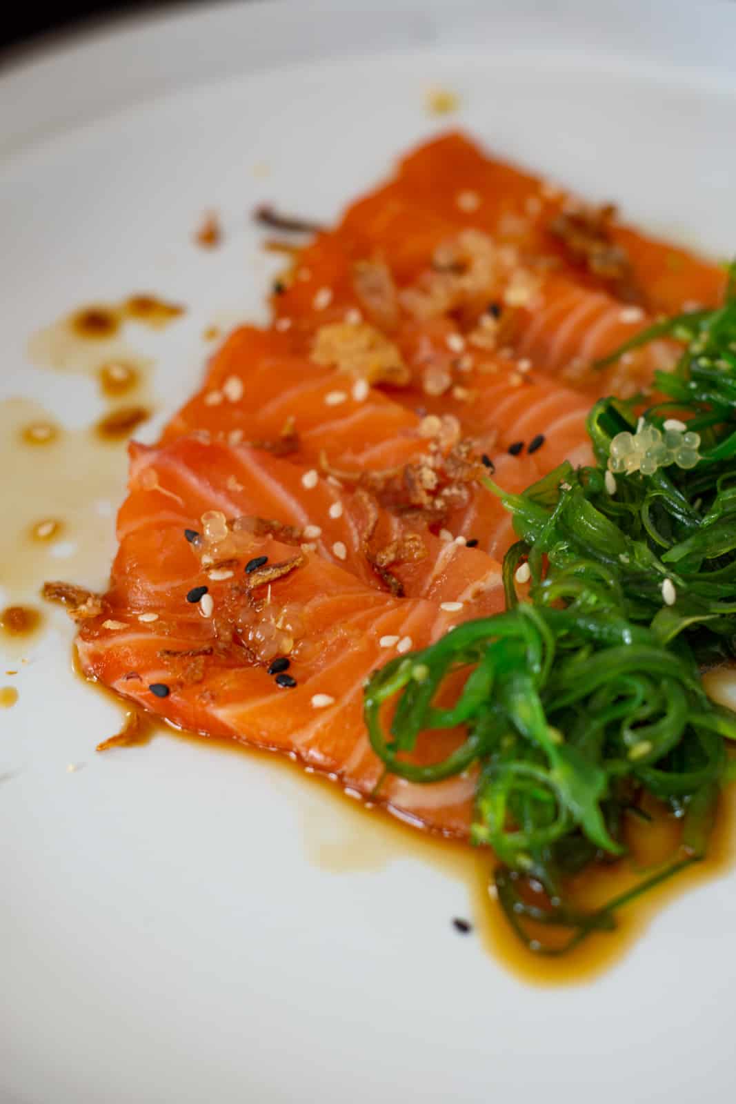 close up of salmon crudo w/ ponzu sauce & wakame on a white plate