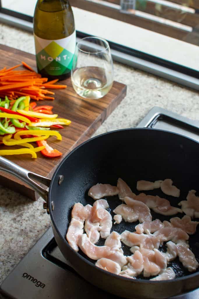 chicken tendeloins in a frying pan with vegetables on a chopping board
