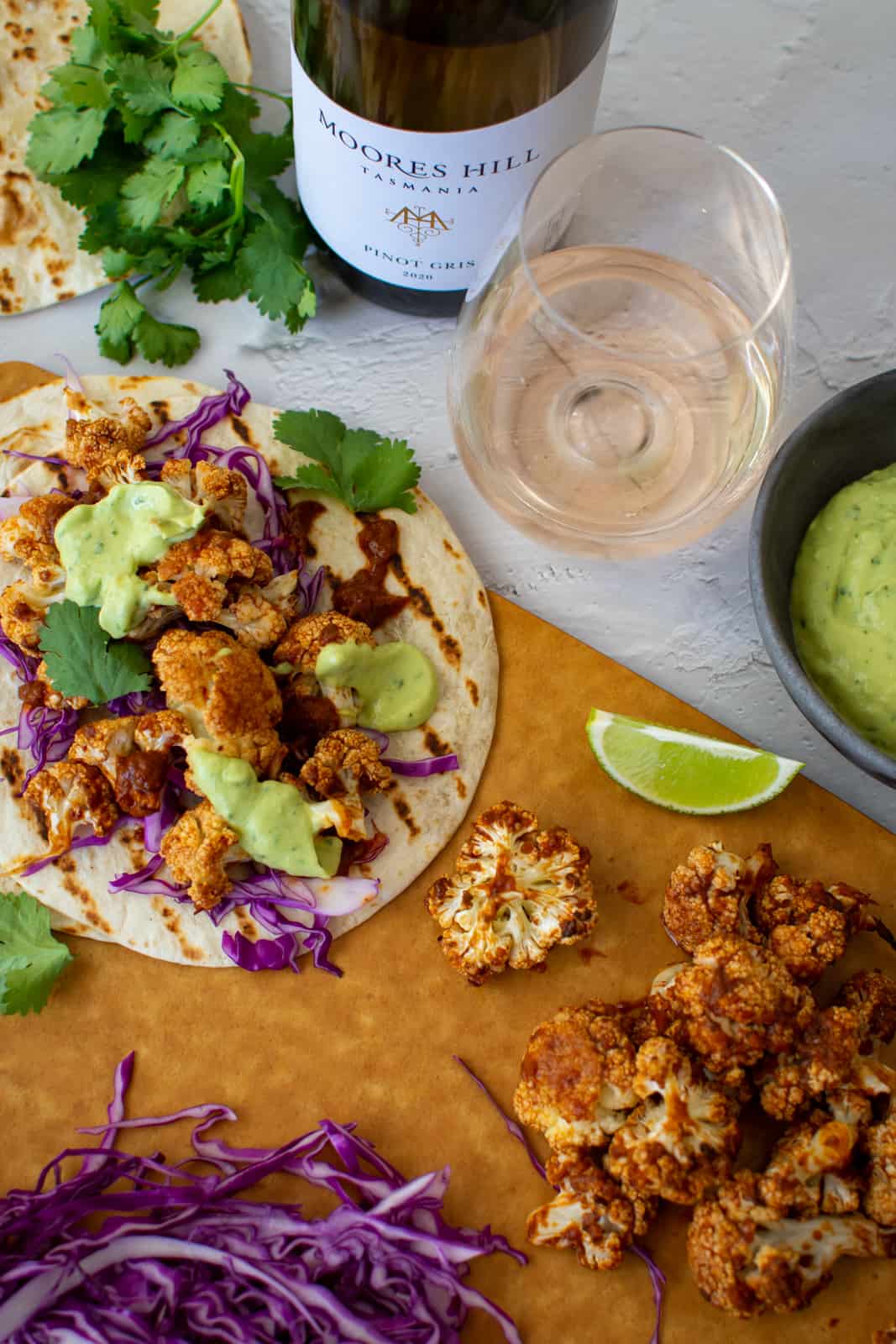 cauliflower taco on a board with roasted cauliflower next to it and moores hill pinot gris