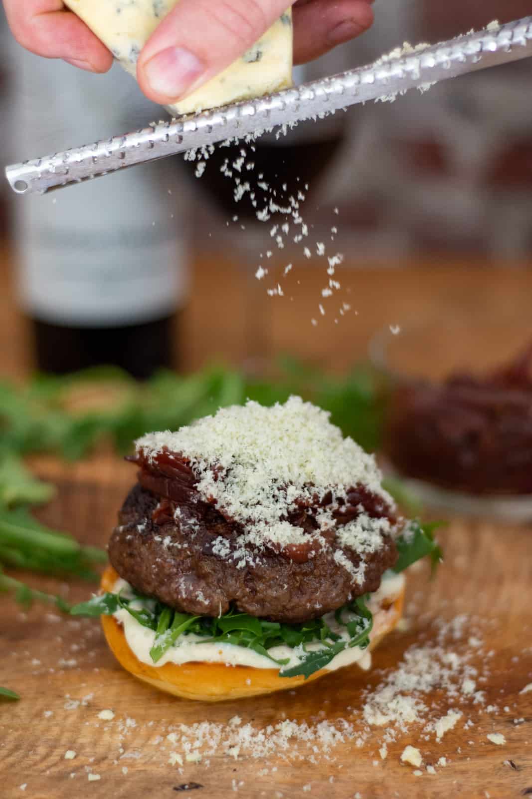 wagyu beef burger on board with frozen blue cheese being grated on top