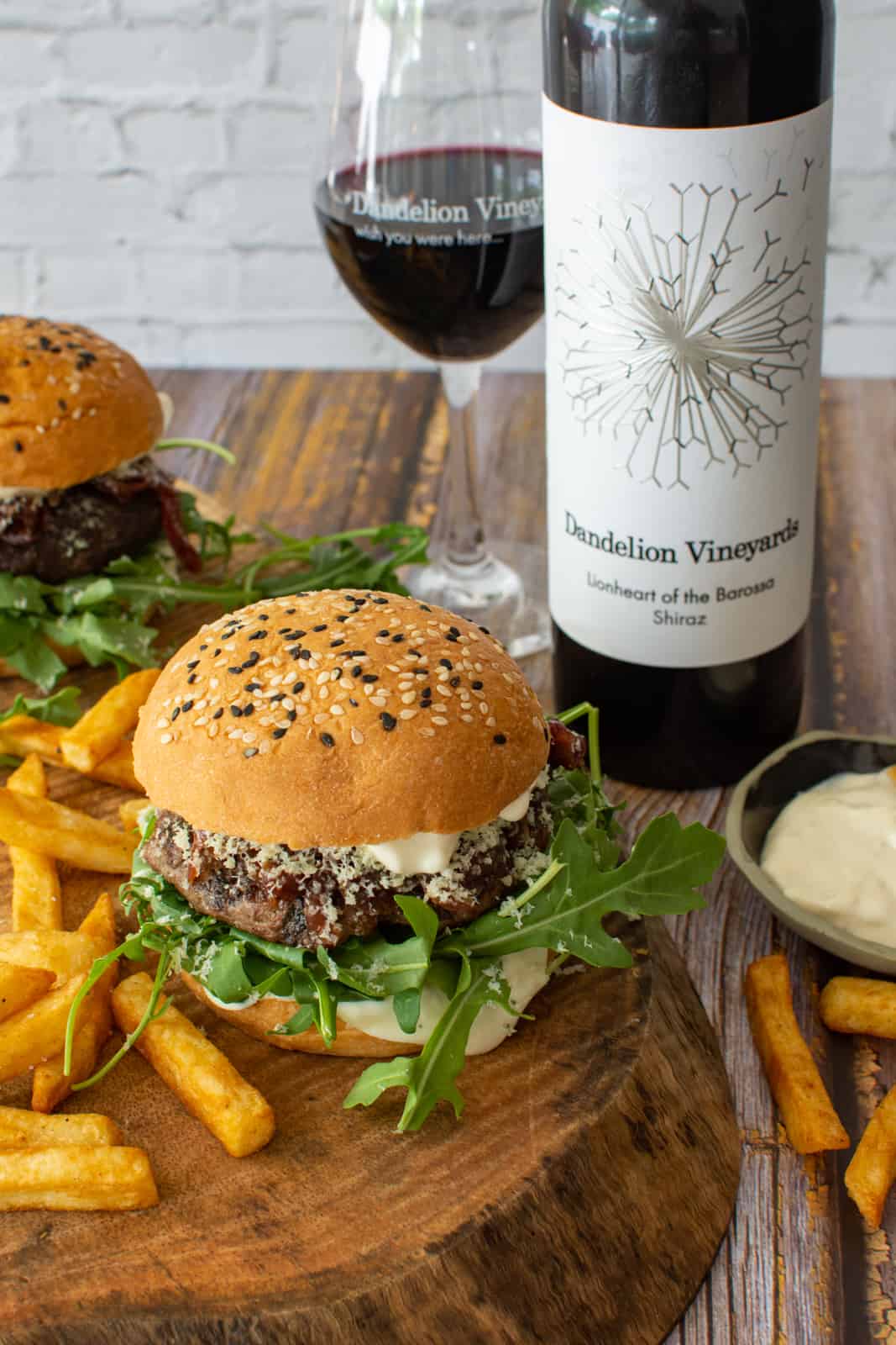 Two wagyu beef burgers on wooden board with chips and bottle of Dandelion lionheart shiraz