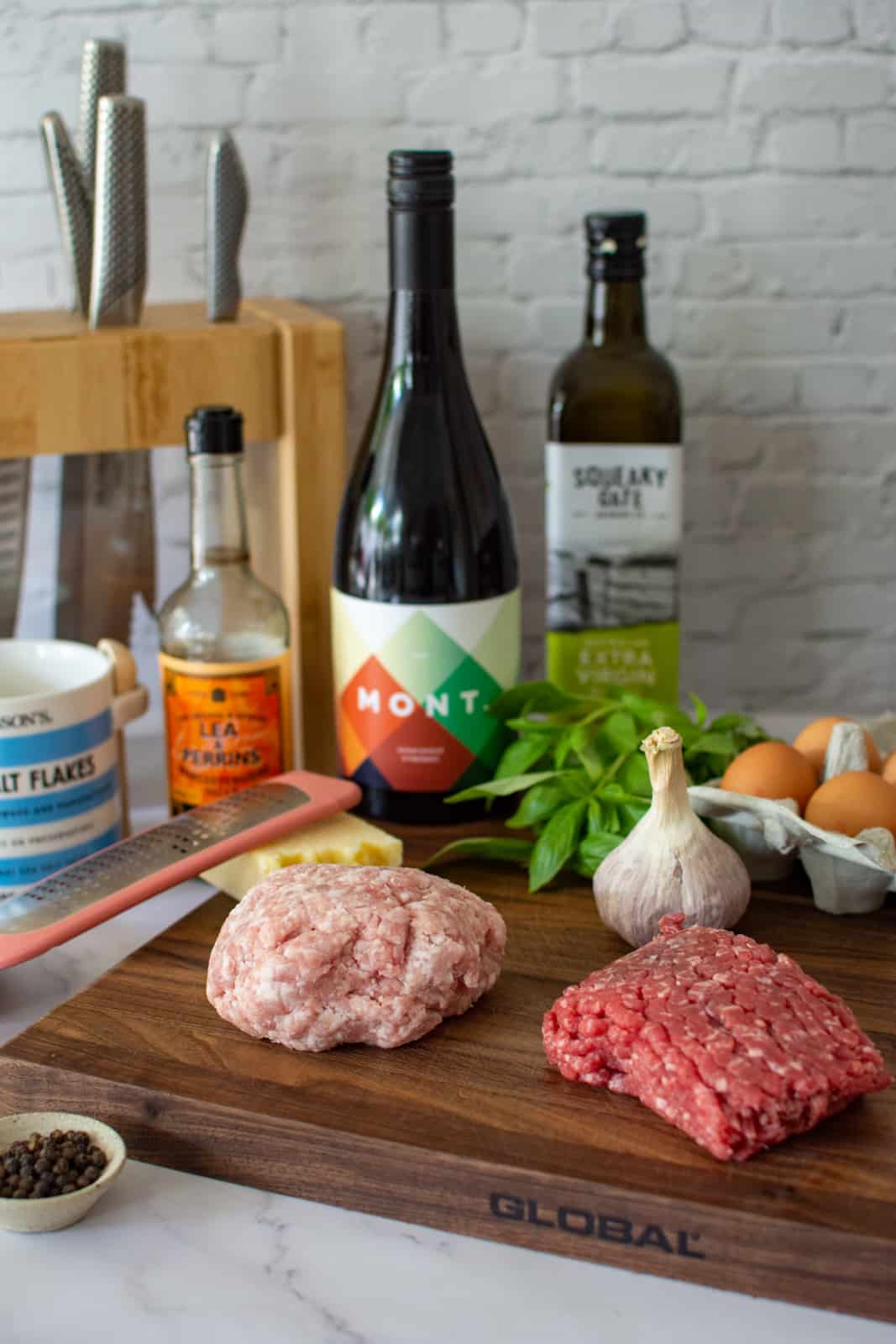 pork & beef mince on a chopping board, mont wine in background and ingredients to make meatballs marinara