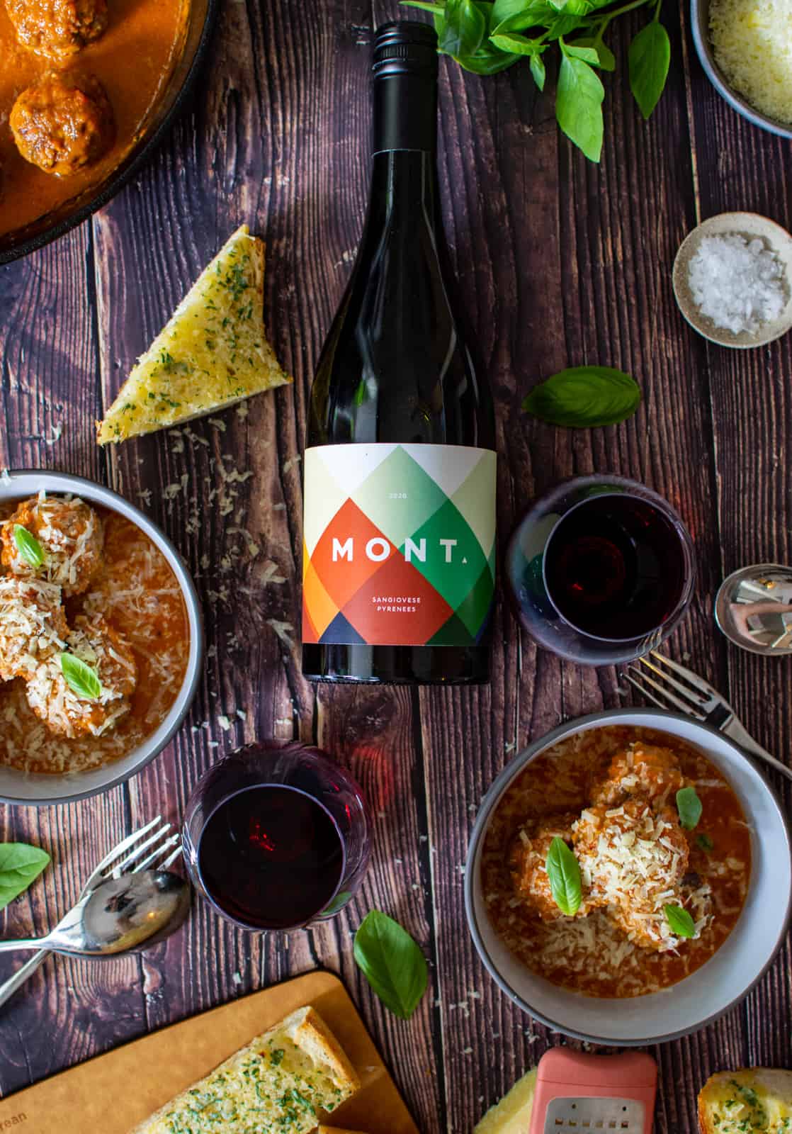 mont sangiovese wine, 2 bowls of meatball marinara & garlic bread on wooden table