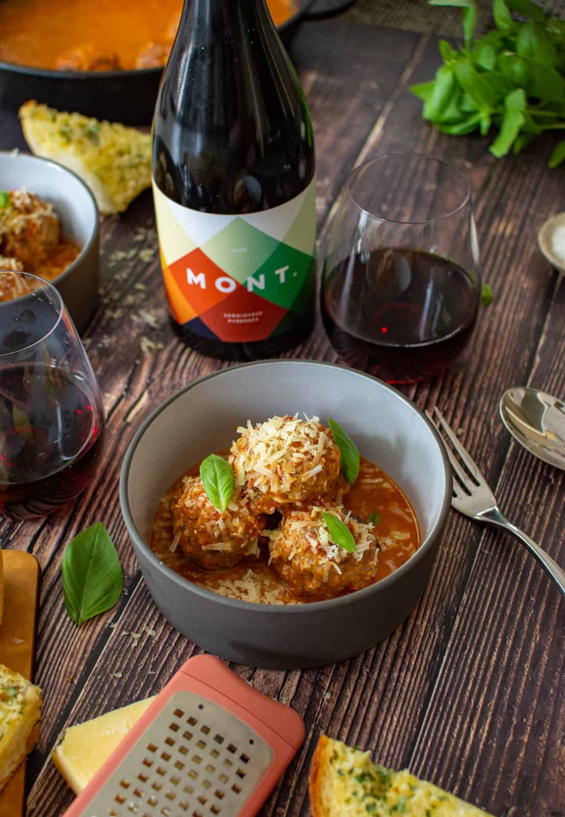 bowl of pork & beef meatballs, marinara sauce, parmsan and some wine in glasses on wooden table