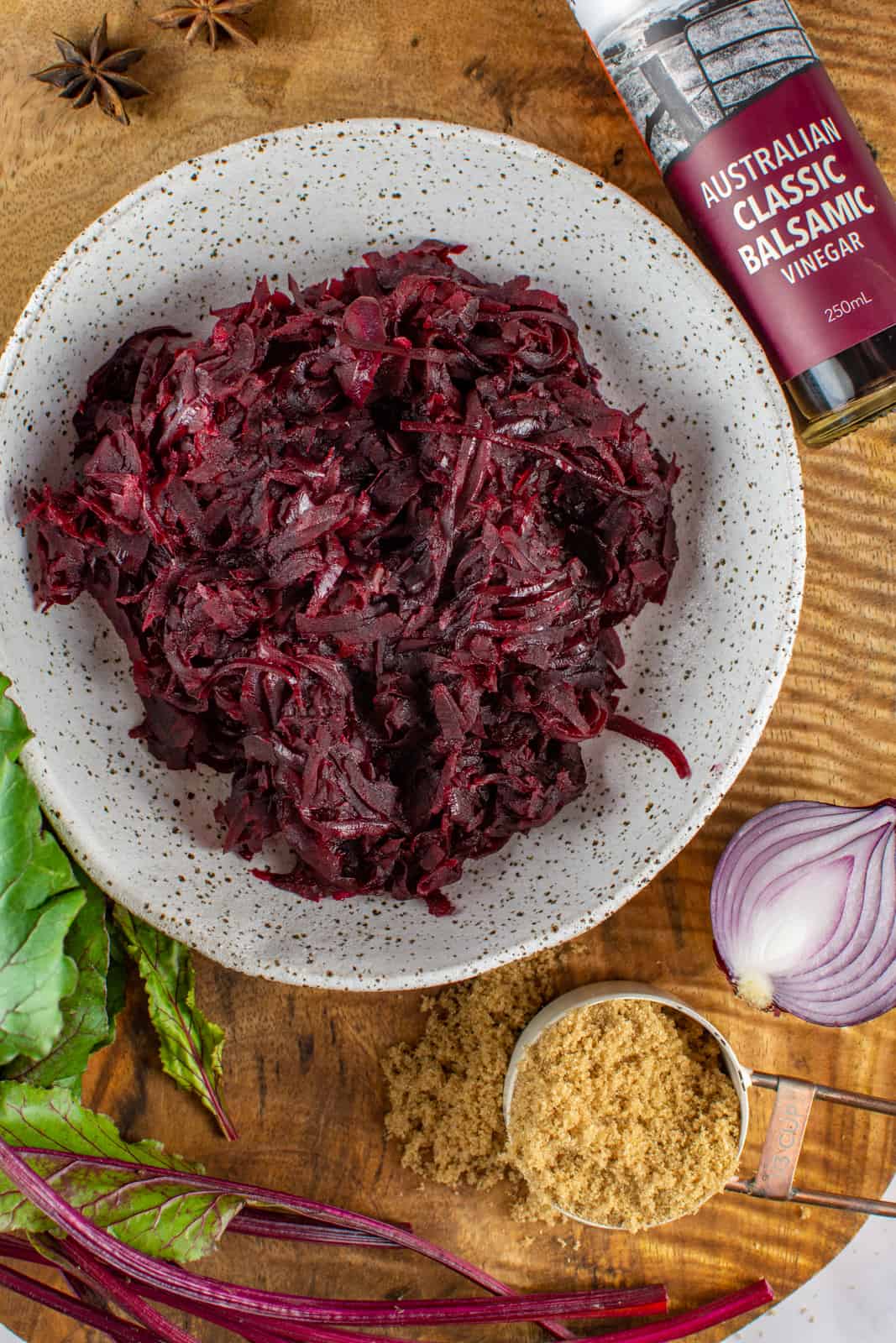 spicy beetroot relish in a white bowl on a wooden board with balsamic vinegar, beets, anise and sugar